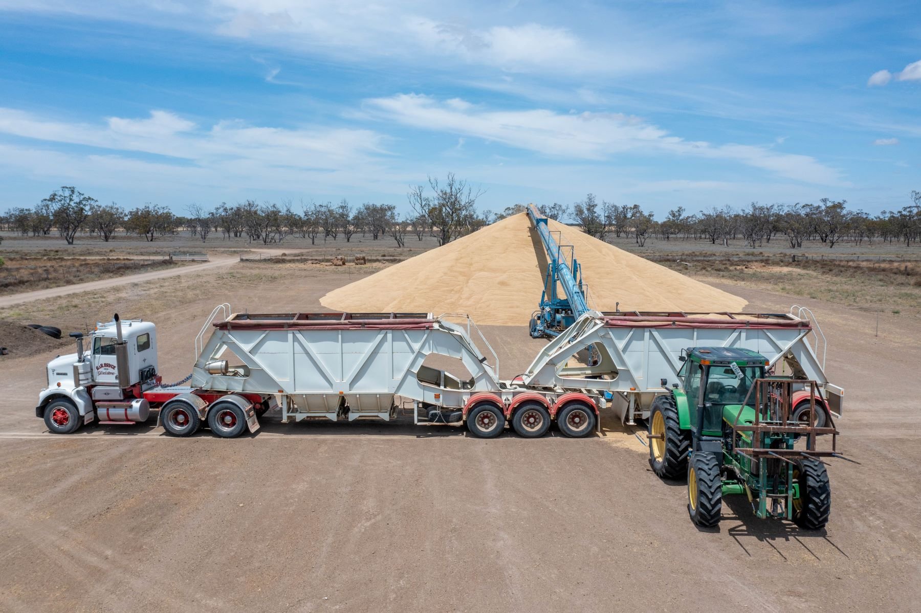 Trucks and tractor loading barley with auger